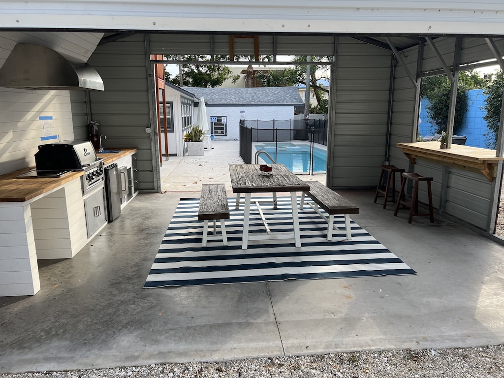 Covered outdoor kitchen area with Blaze BBQ gas grill, sink, dining table and bar top.