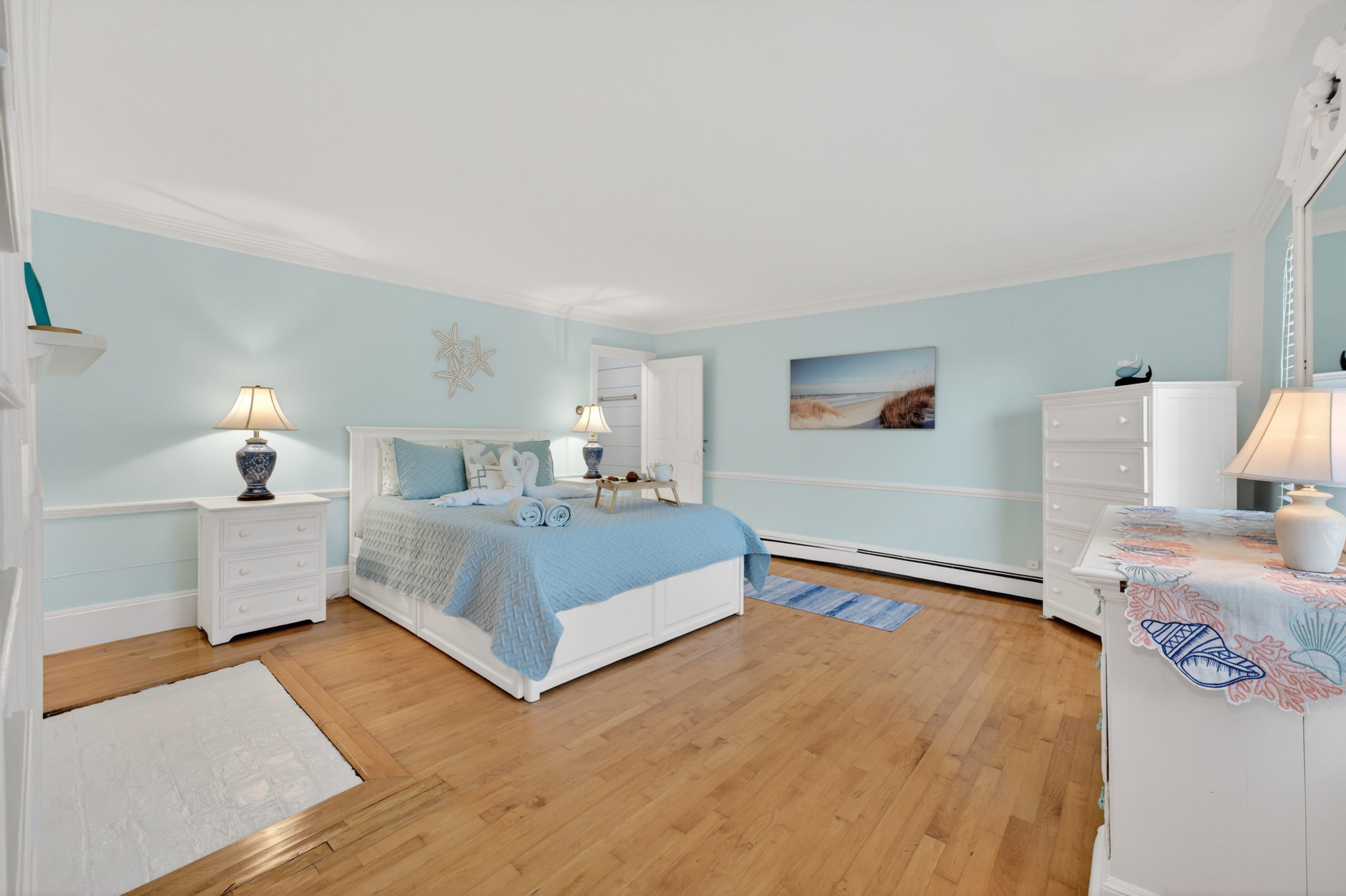 Bright and airy primary suite with a comfortable bed, hardwood floors, and relaxing coastal touches.