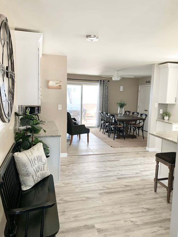 Enjoy the spacious feel of our open-concept home. The view from the entryway reveals a seamless flow from the stylish coffee station to the large farmhouse dining table, all flooded with natural light from the sliding glass doors.