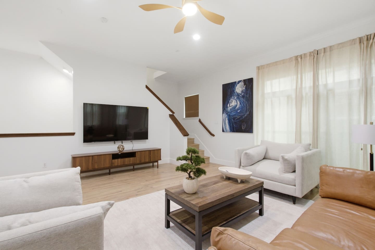 Smart TV, spacious sectional seating, and a clean sightline through to the kitchen and staircase. The kind of living room that actually fits a full group comfortably.

