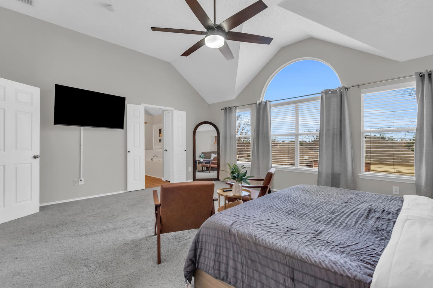 Well-appointed primary suite with a king bed, TV with streaming,  full length mirror, seating area, modern art accents, room-darkening shades, and climate comfort for quality sleep.