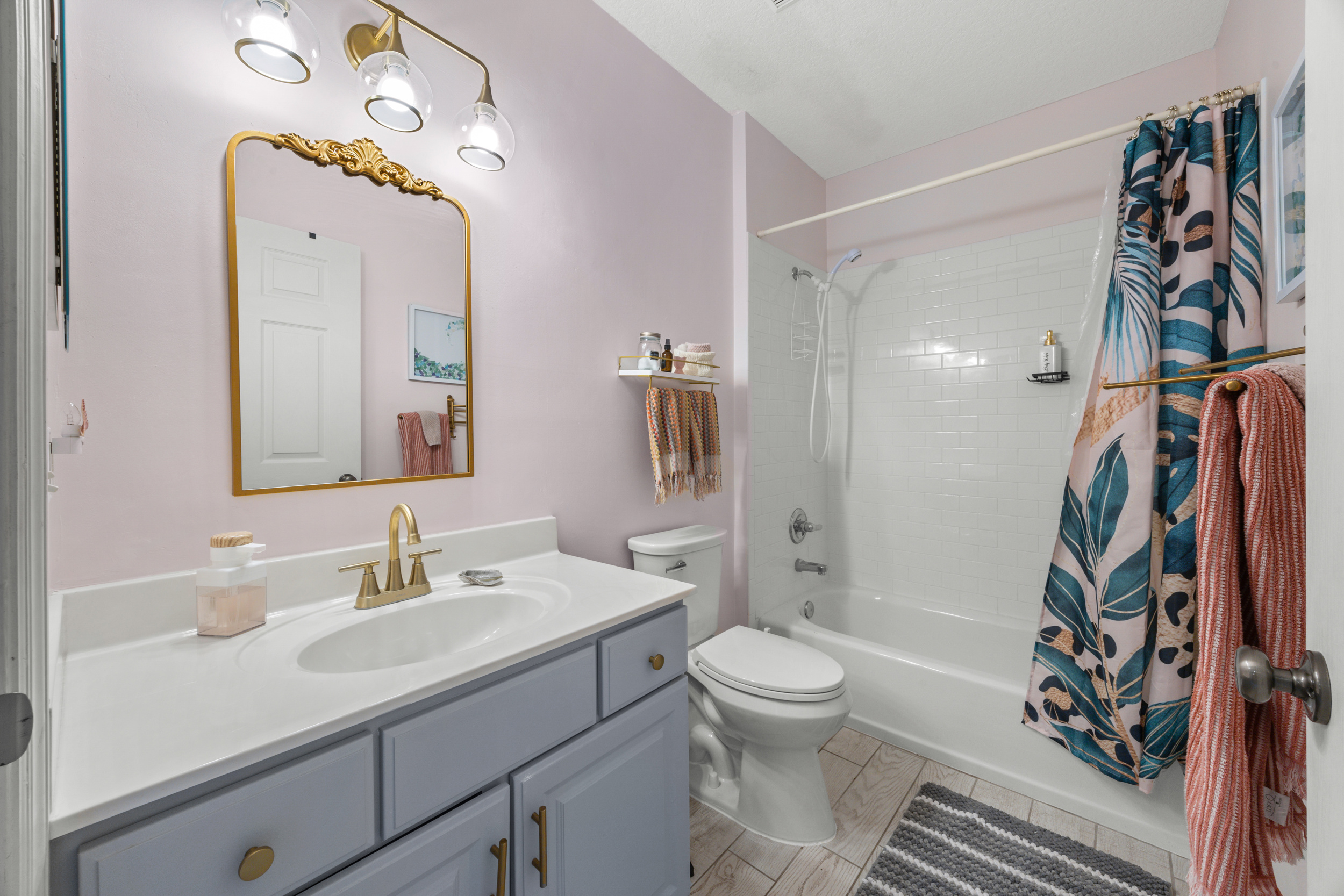 Beautifully updated bathroom with gold accents, subway‑tile shower, and a colorful botanical curtain.