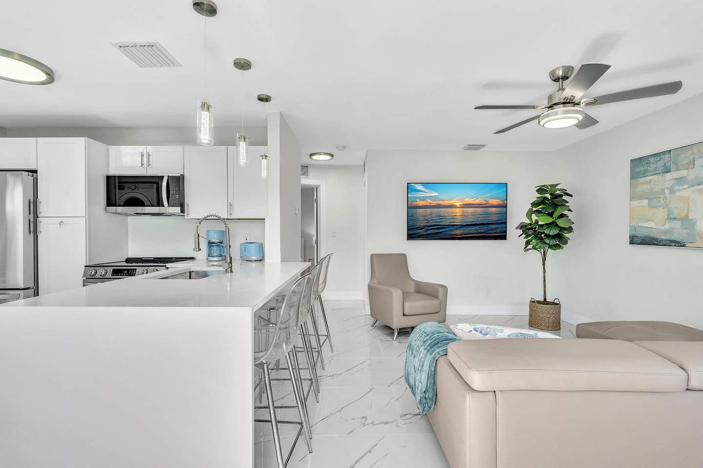 Open-concept living room and kitchen with comfortable seating, a large TV, breakfast-bar seating, and a fully equipped kitchen with stainless steel LG appliances.