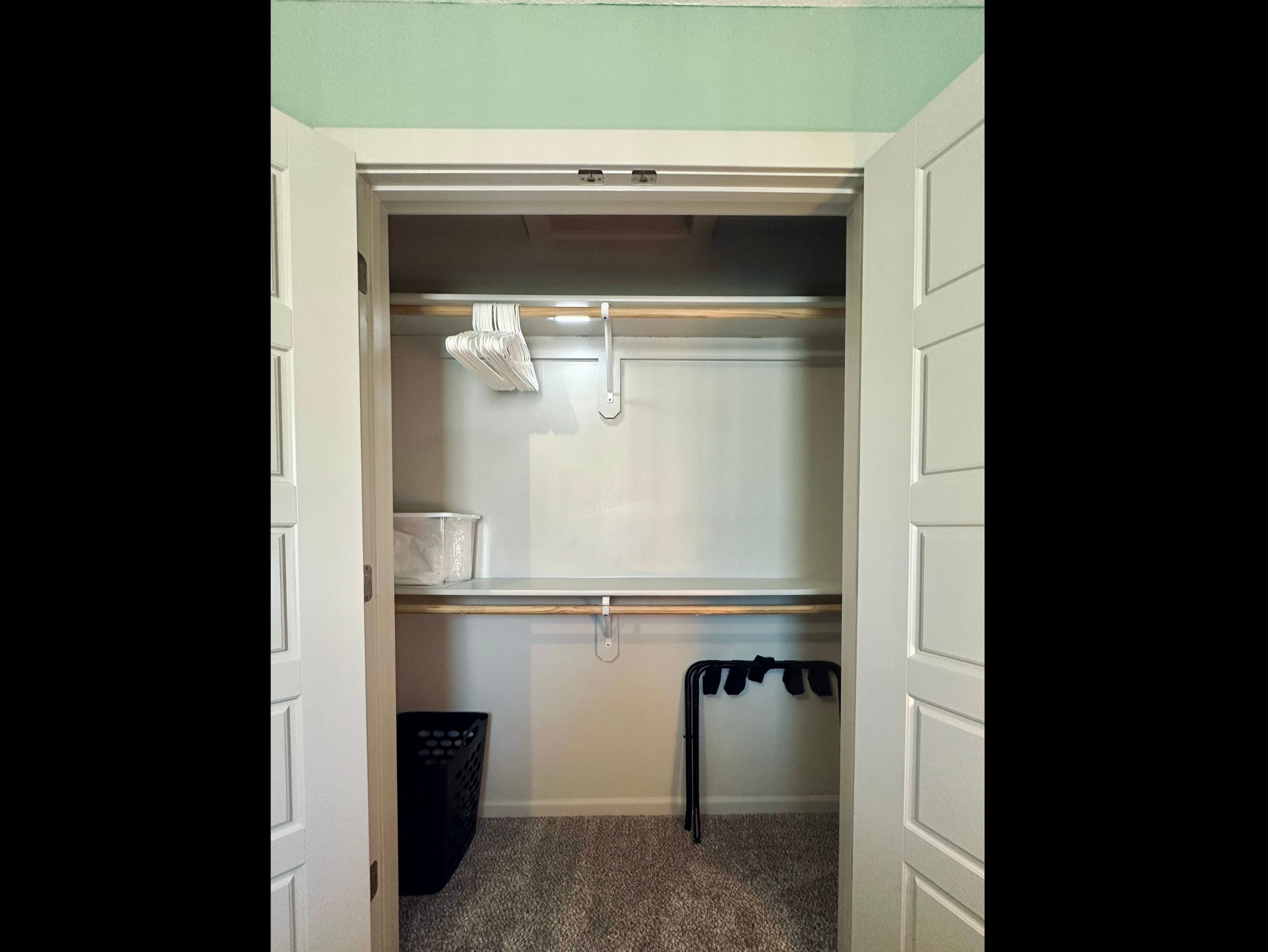 Queen bedroom closet thoughtfully equipped with hangers, luggage rack, extra linens, and laundry basket for a comfortable stay.