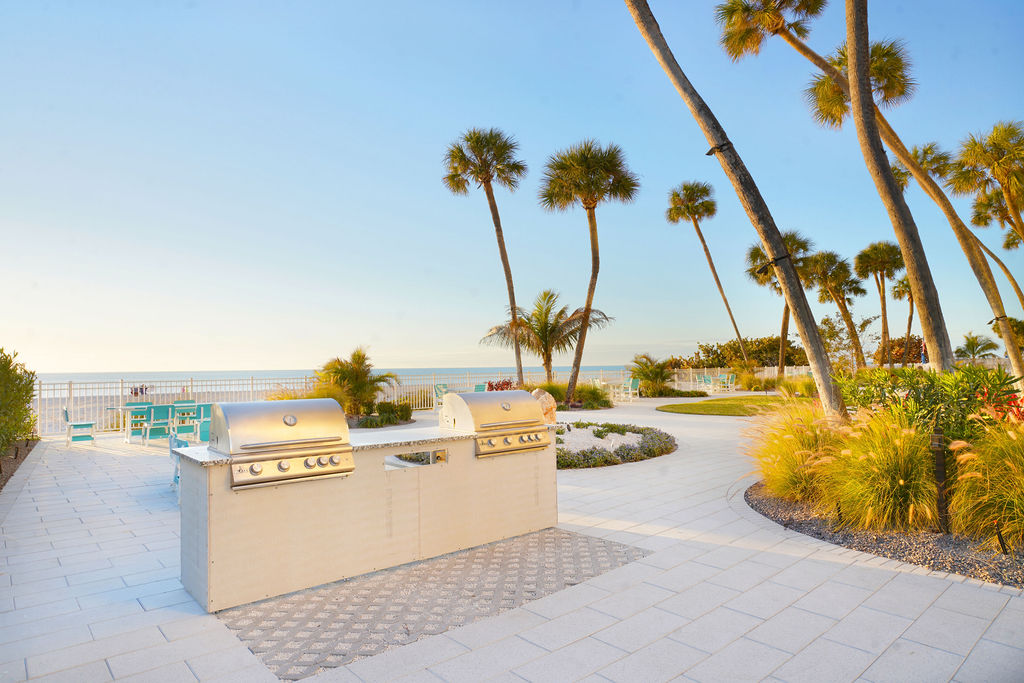 Community grilling area with premium BBQ grills, tropical landscaping, and outdoor dining space, perfect for beachside cookouts and sunset gatherings.
