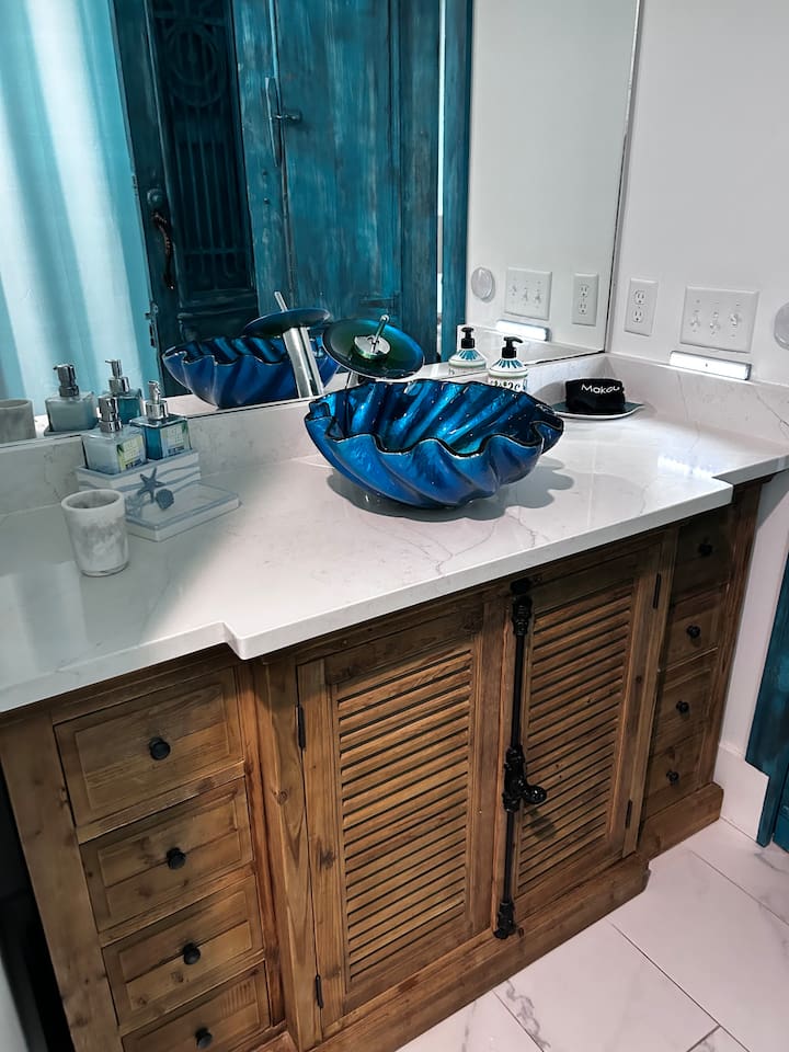 Artisan Charm: One-of-a-kind antique cabinet with industrial bolt detailing, topped with a whimsical shell sink. A custom touch of coastal elegance in the main bath.