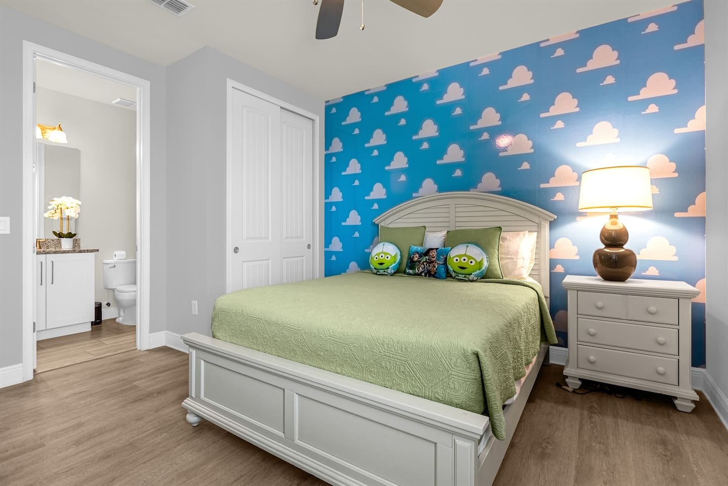 The room is a playful homage to the beloved "Toy Story" franchise, bursting with bright colors and nostalgic decor. The walls are painted a soft sky blue, adorned with large, cartoonish clouds reminiscent of the iconic wallpaper from Andy’s room.