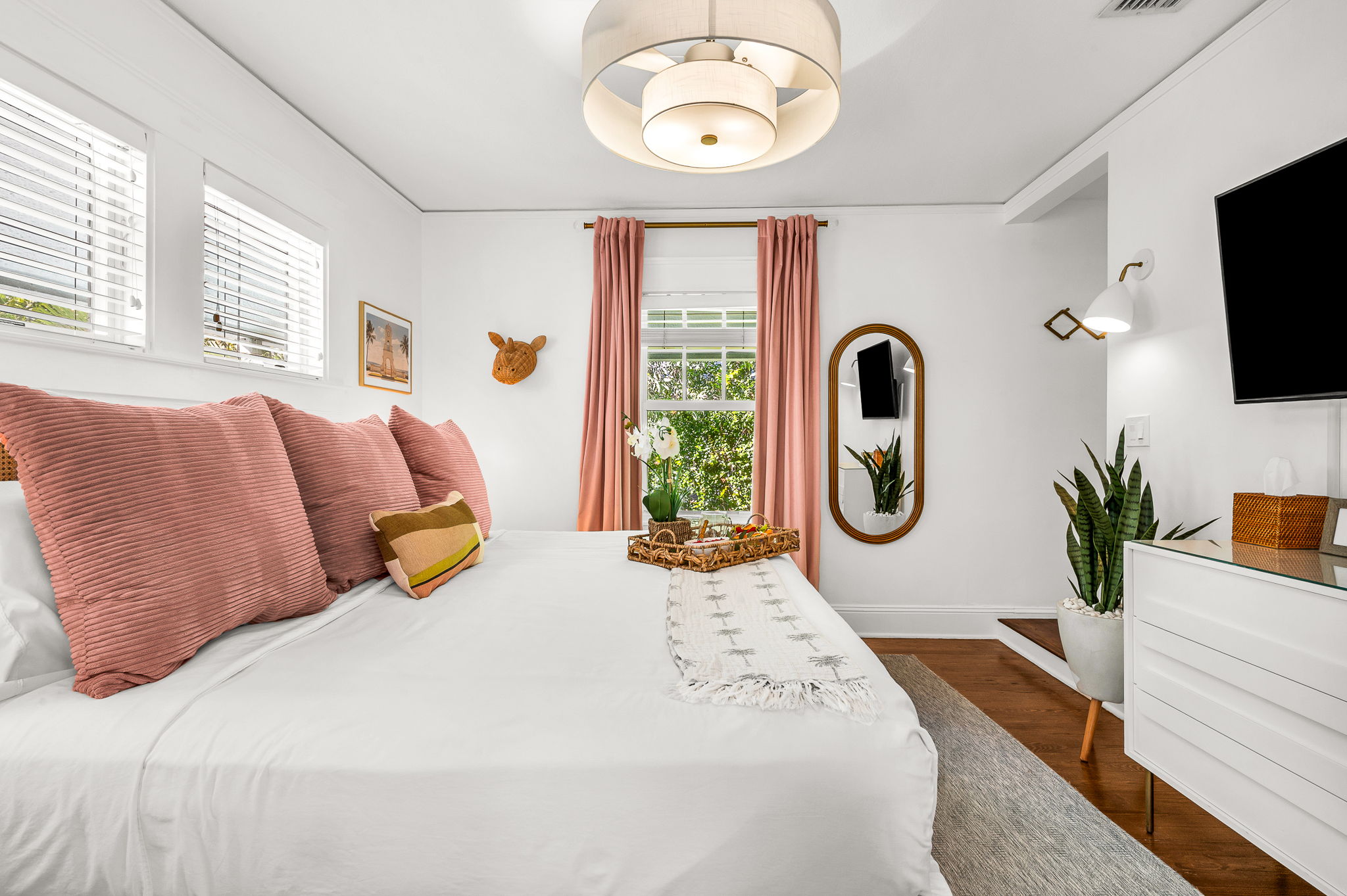 Primary bedroom with a king bed, smart TV, and ensuite bath featuring an antique soaking tub and modern shower. Cane rattan headboard, blackout drapes, and Palm Beach art add charm. Opens to the 4th bedroom, ideal for a private family suite.