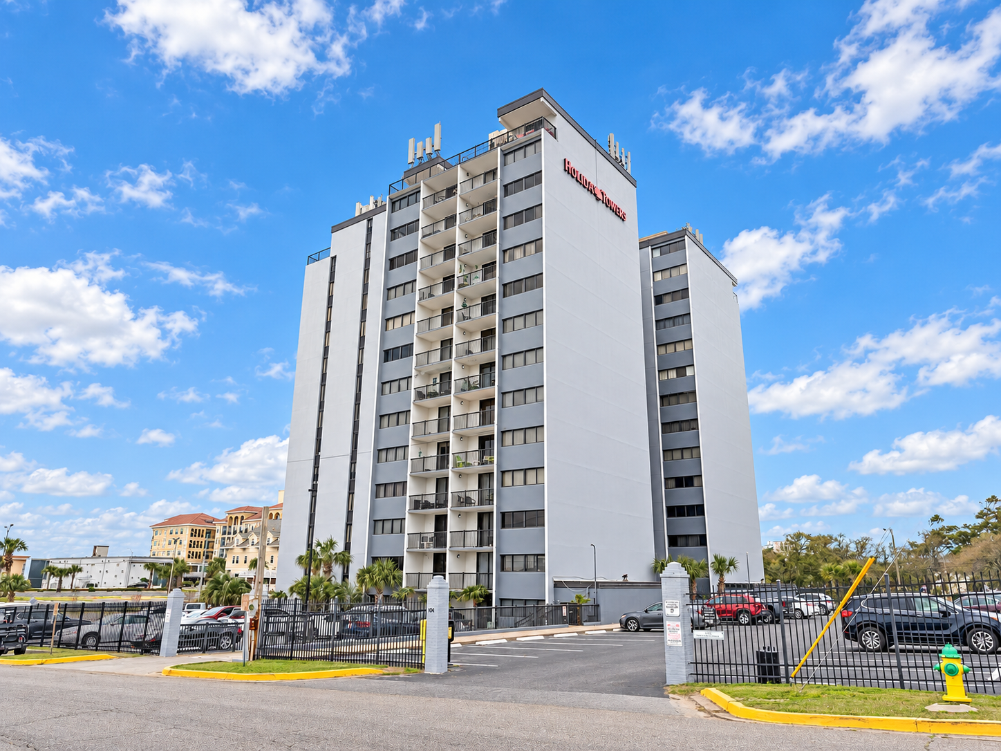 Aerial view of Holiday Towers with shared pool, hot tub, sports court, parking, and Myrtle Beach attractions nearby.