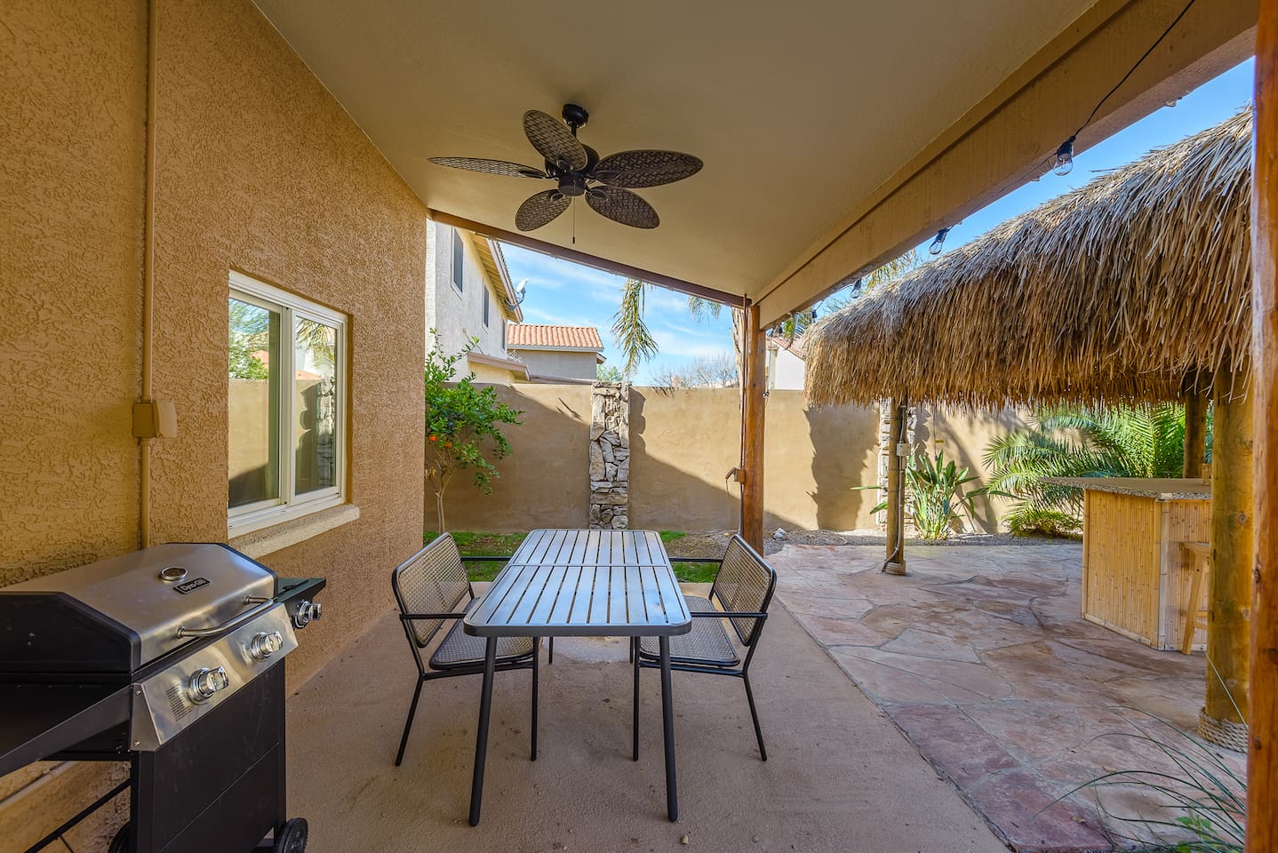 Covered patio dining area with BBQ grill, pool views, and easy access to the tiki lounge and backyard seating.