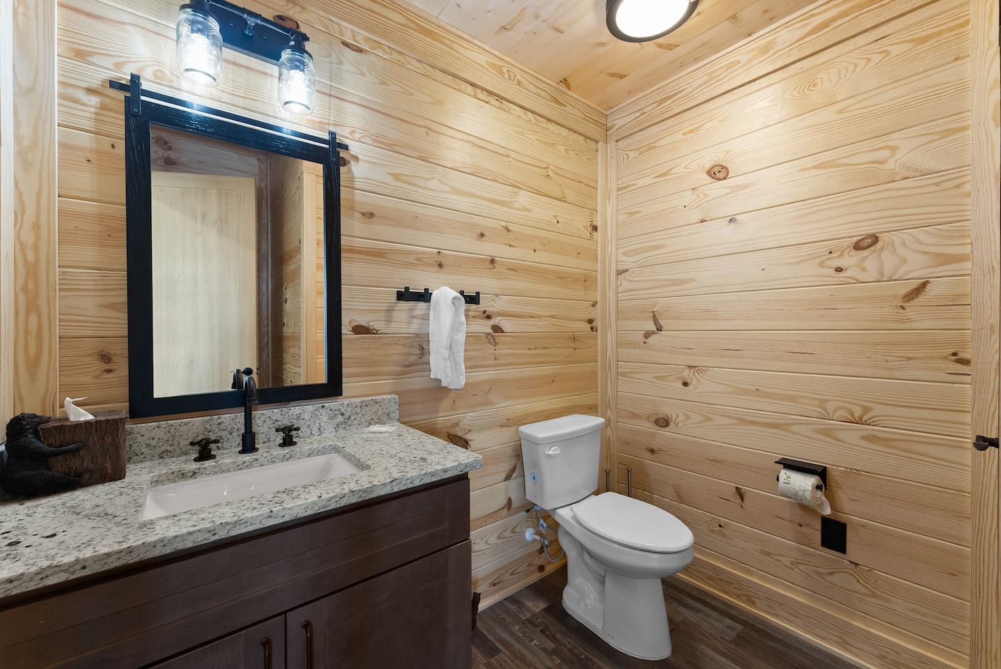 Rustic charm meets functionality in this stylish half bath, featuring a granite countertop, wood-paneled walls, and modern black fixtures.