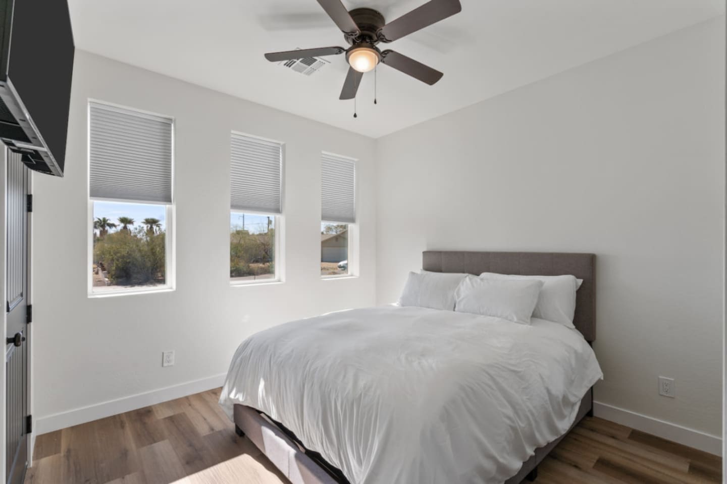 Bright guest bedroom with a comfortable bed, wall-mounted TV, and plenty of natural light.