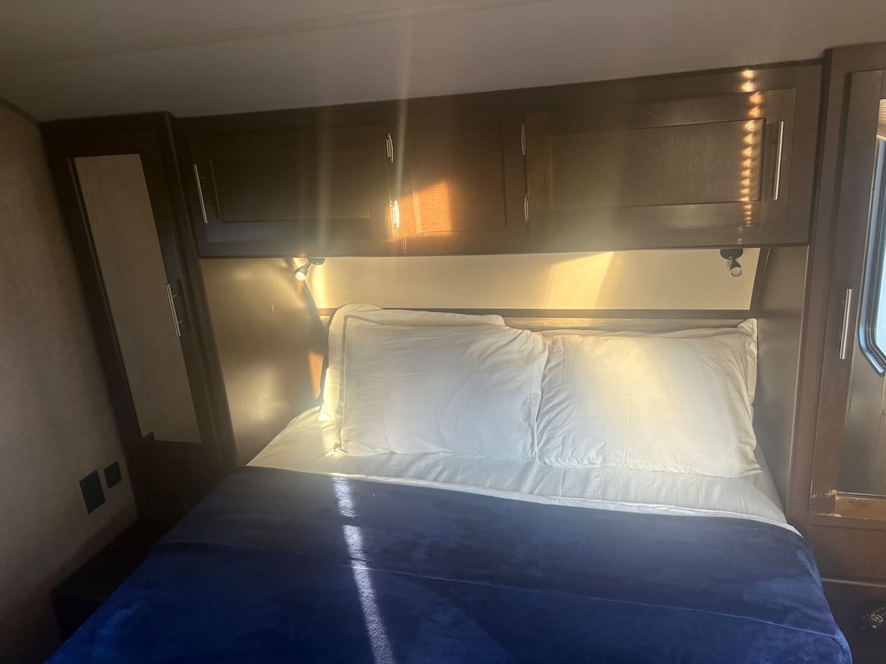 Queen size bed with four pillows. Bathroom towels are stored in the cabinet above bed.