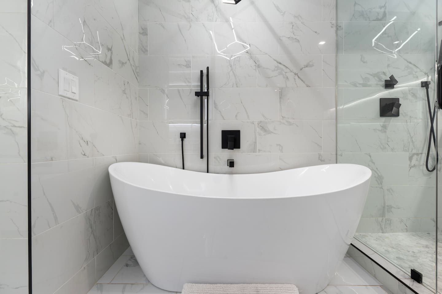 Freestanding tub surrounded by sleek marble tile and matte black fixtures.

