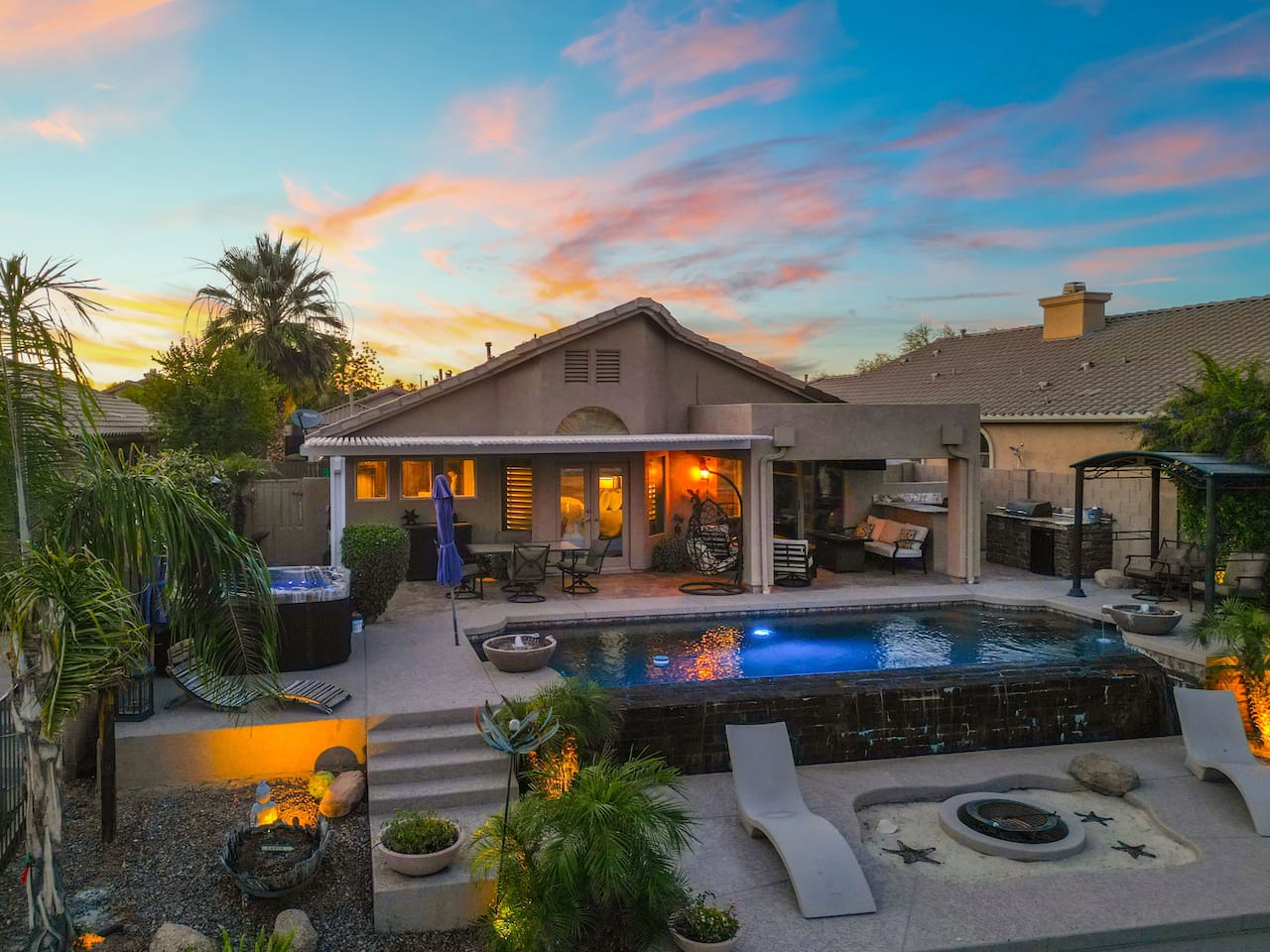 Every corner of this backyard has something to offer — hot tub, pool, fire pit, outdoor kitchen, and a covered lounge — all bathed in the warm glow of a stunning desert sunset.
