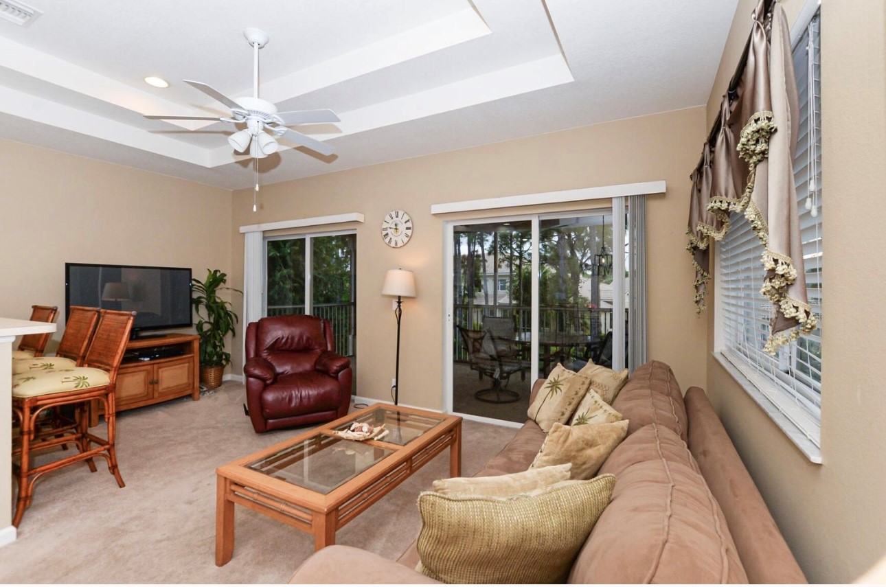 Comfortable living area with cozy seating, large windows, tile flooring, and direct access to the screened balcony.