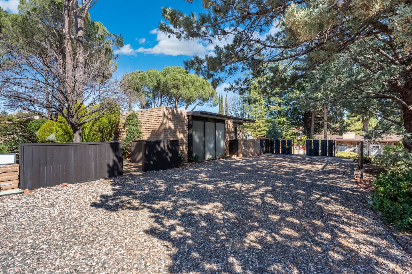 Private gated entrance with spacious gravel drive, surrounded by mature trees and lush desert landscaping for added seclusion.