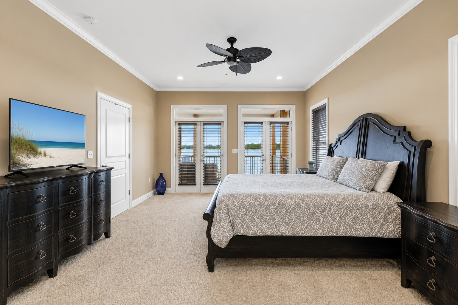 Spacious bedroom with dark wood furnishings, smart TV, and private balcony doors framing the lagoon