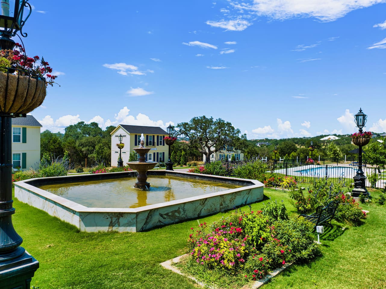 Stroll through manicured gardens centered around a classic fountain, with rolling hills and blue skies as your backdrop.