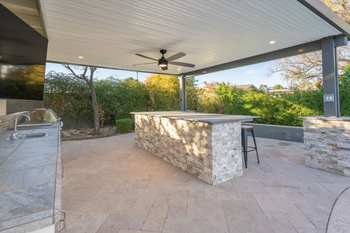 A stone-clad bar counter offers plenty of space to gather outdoors, shaded and ready for entertaining.