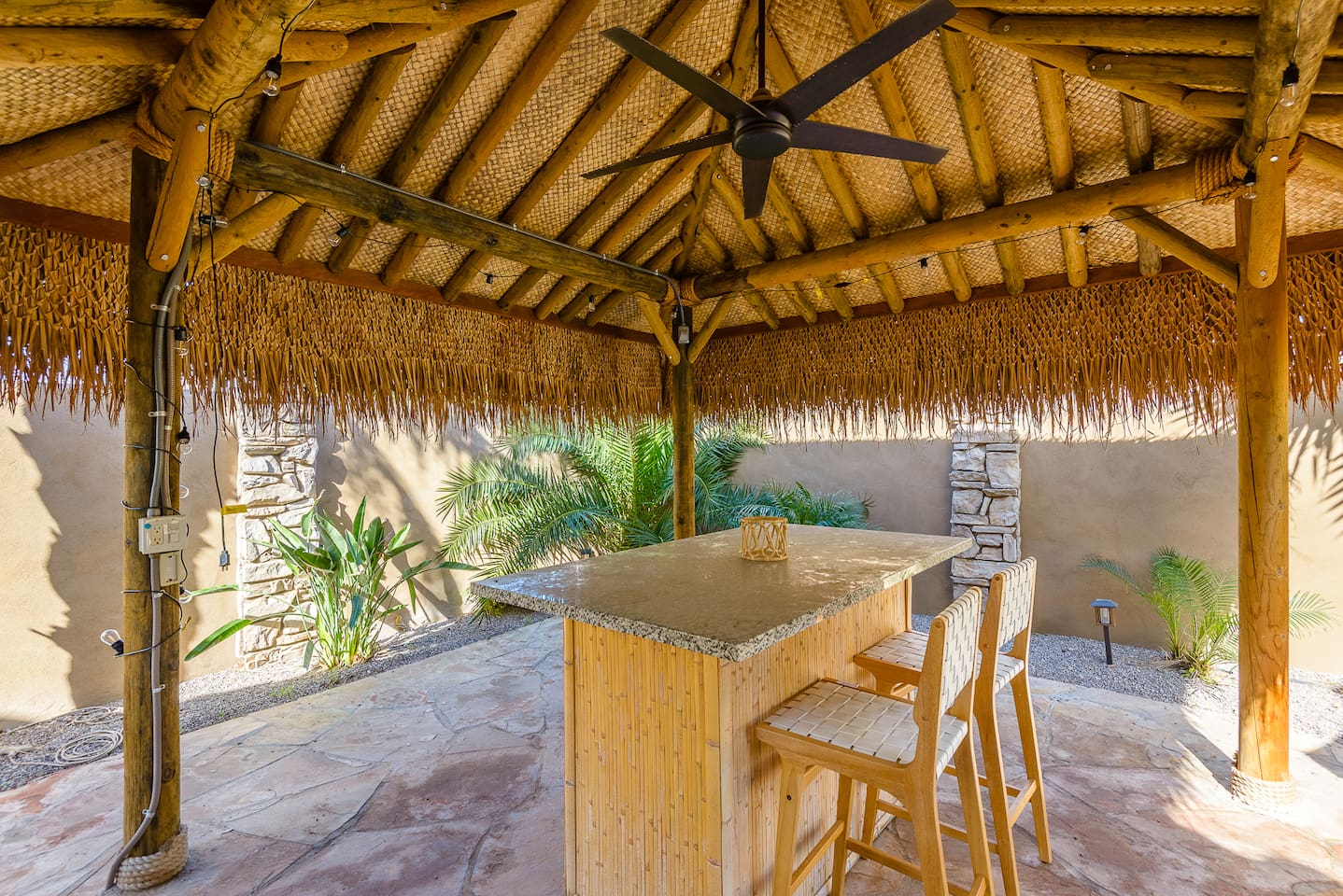 Outdoor tiki pergola lounge with bar seating, ceiling fan, and a shaded spot to relax by the pool.