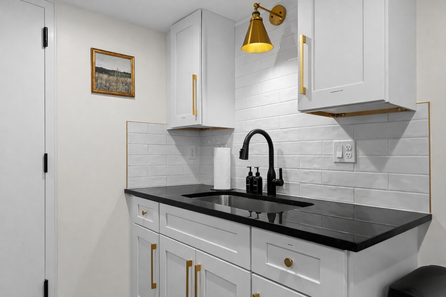 Sleek, modern kitchenette with crisp white cabinetry, bold black countertops, and elegant brass accents—perfect for effortless meals and a polished stay.