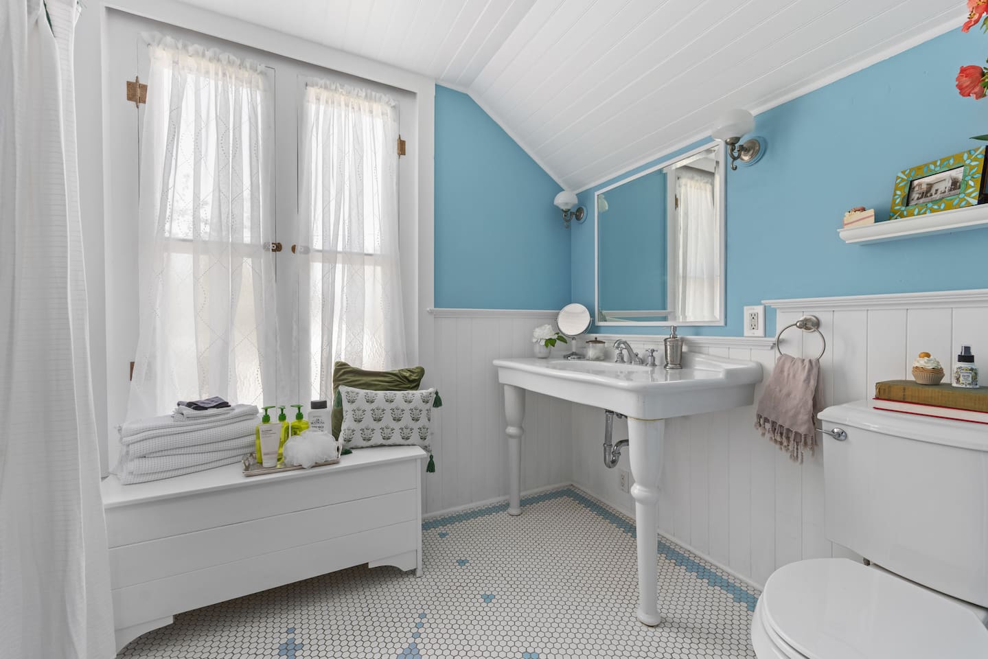 Shared by both upstairs bedrooms, this sunlit full bath is stocked with fresh towels and bath essentials. Playful tile mosaic and reading material joins the fun, with books on Marie Antoinette and her infamous "Eat Cake" line.