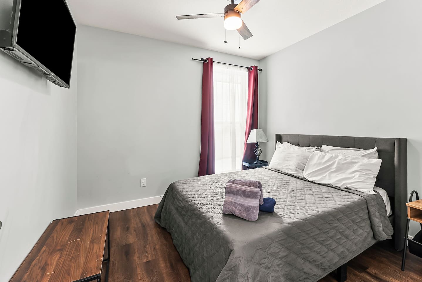 Comfortable second bedroom featuring a full-size bed, ceiling fan, and wall-mounted TV for relaxing evenings.