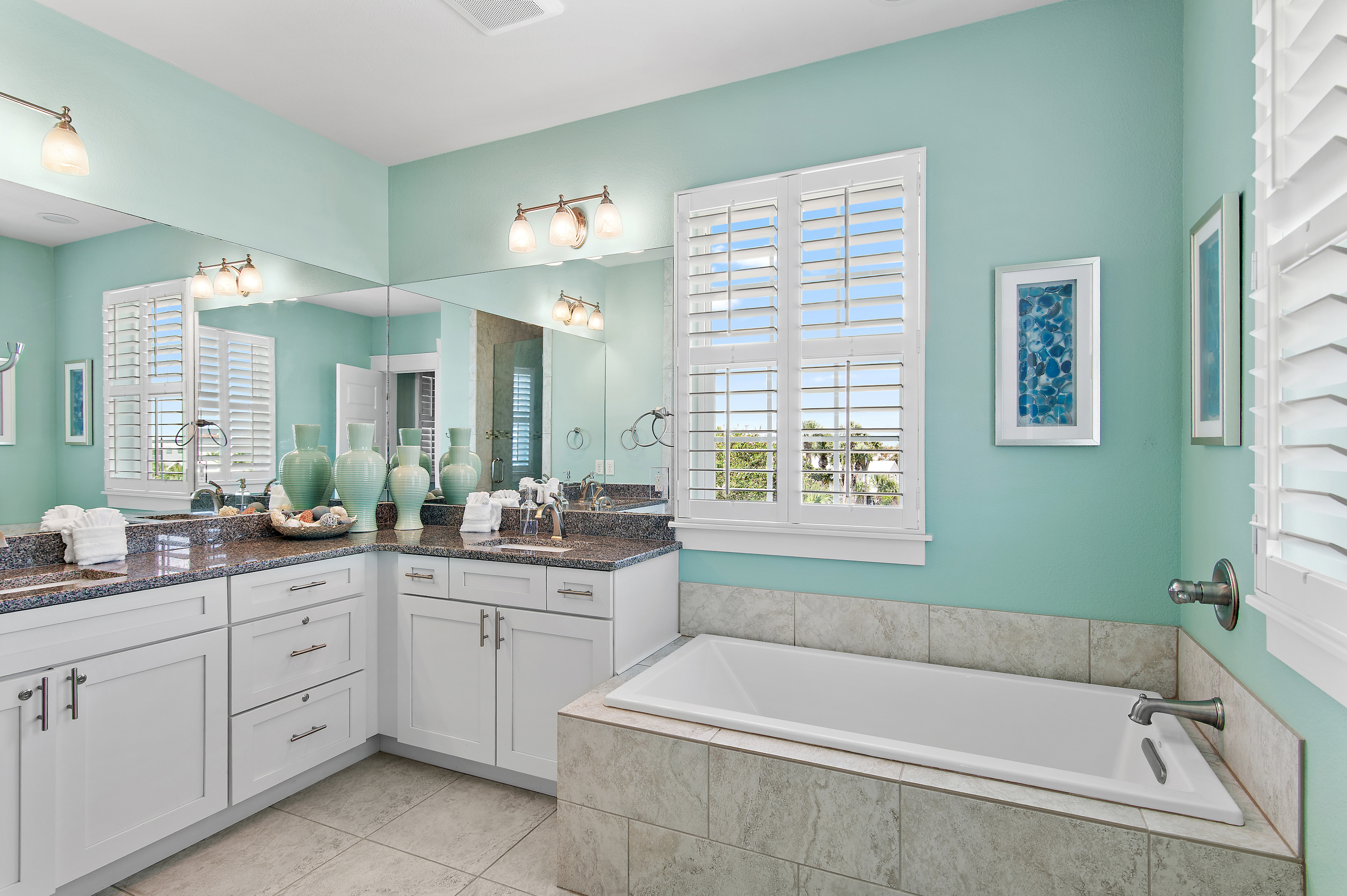 Bright, spacious bathroom featuring a relaxing soaking tub, dual vanities, and beautiful coastal details.
