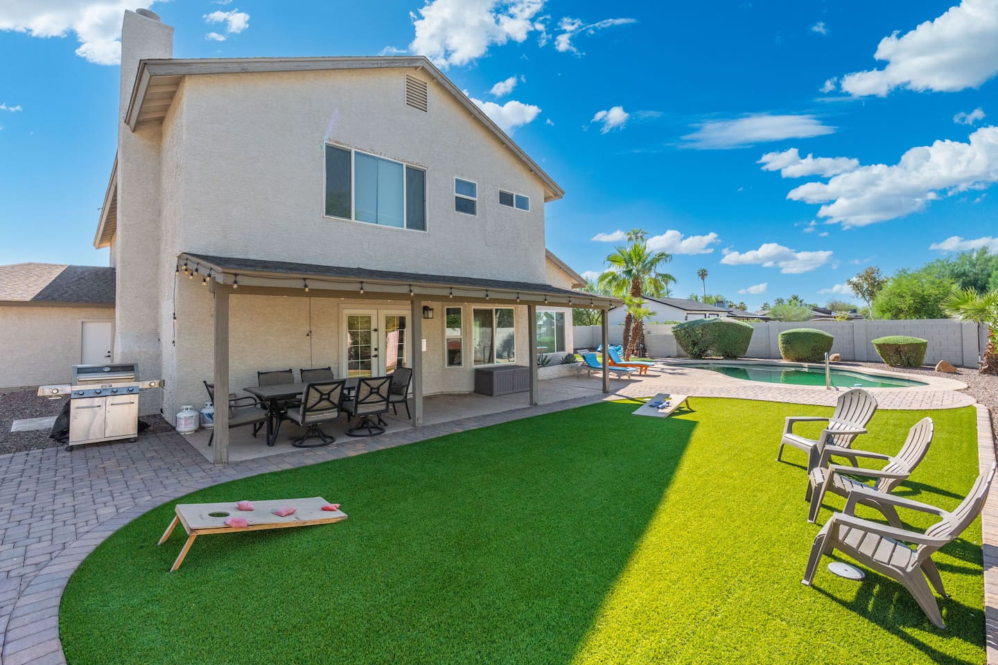 Modern home with expansive lawn, covered patio, outdoor kitchen, and sparkling pool—perfect for entertaining and games.