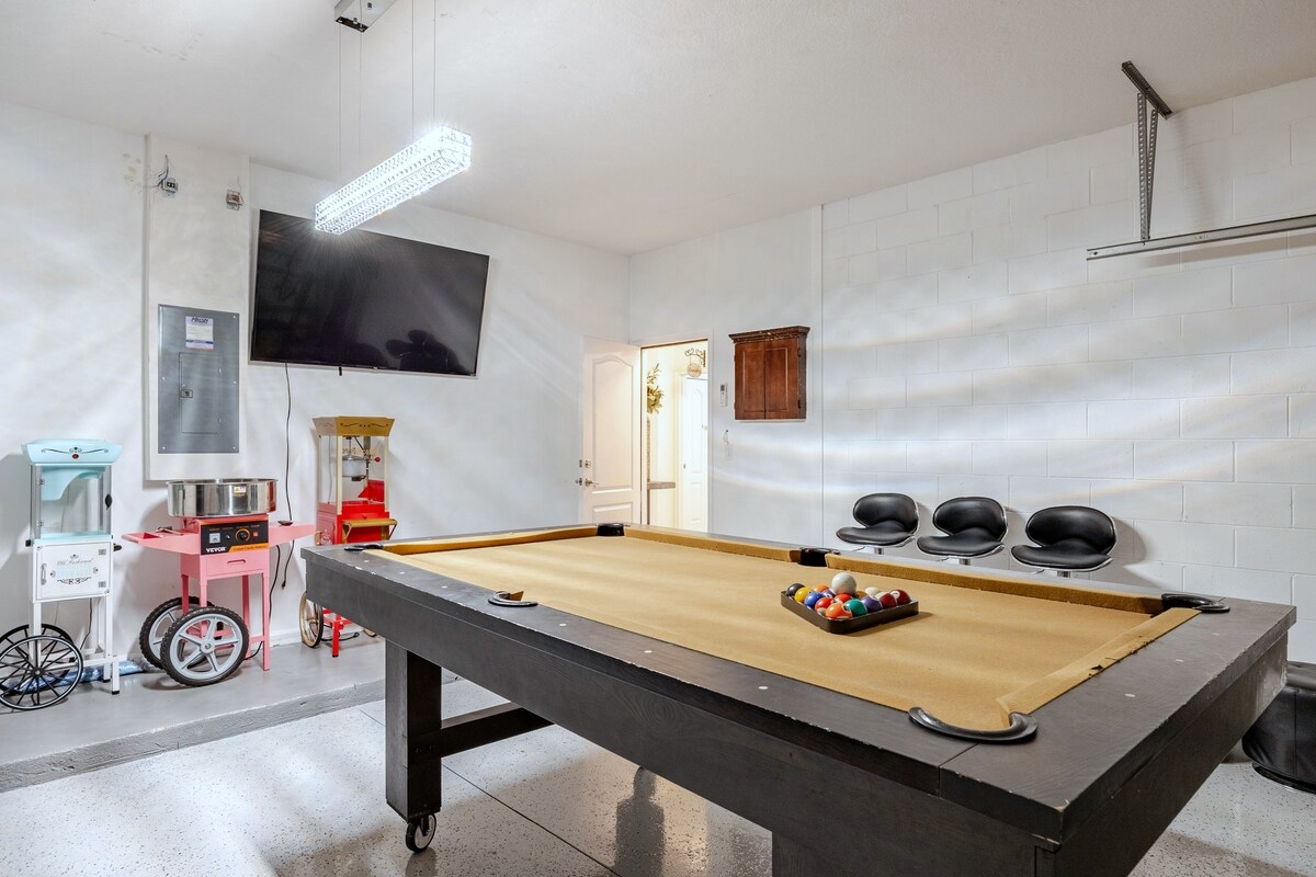 Garage game room with a pool table, TV, seating and popcorn, cotton candy and snow cone carts.