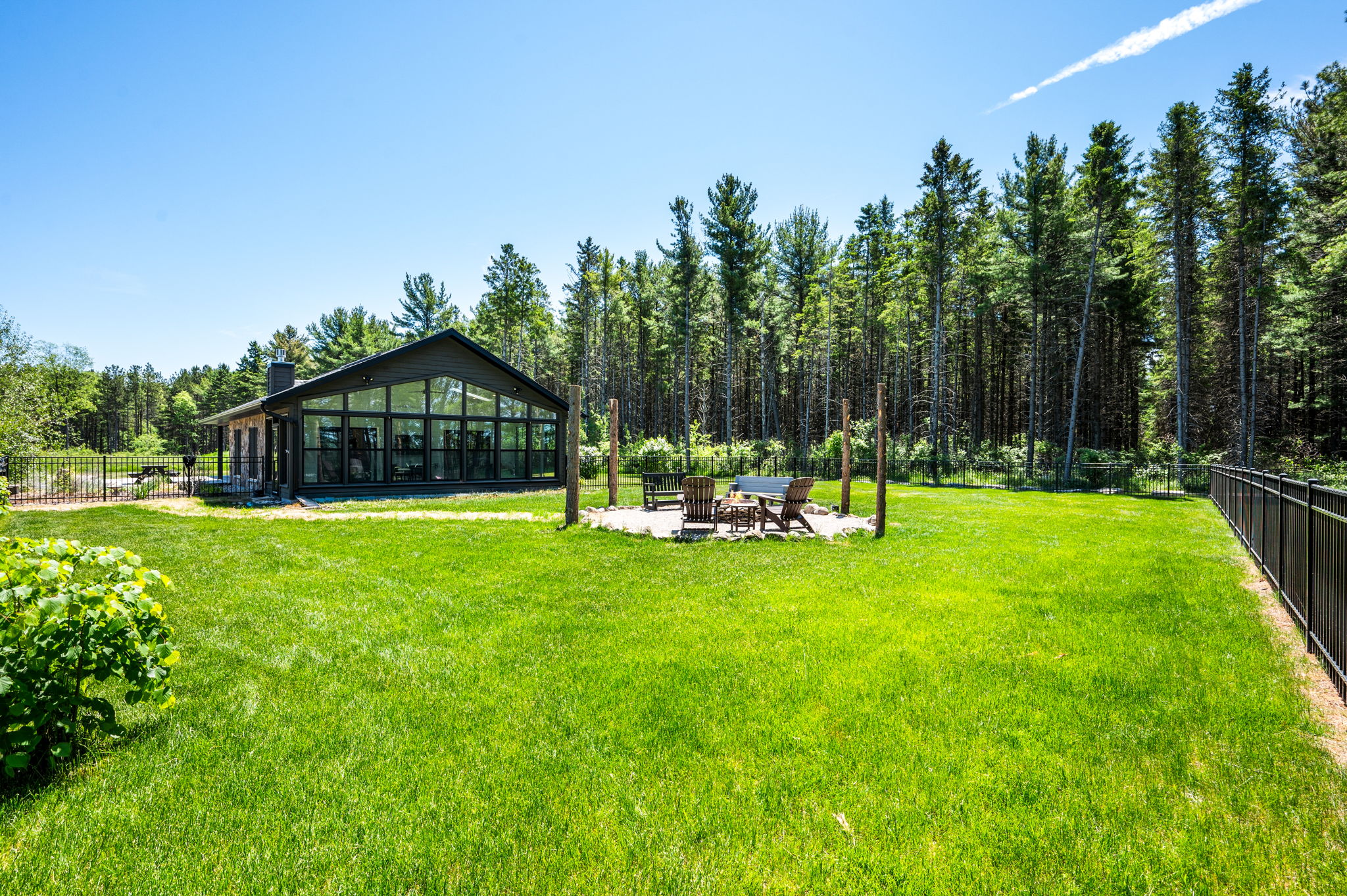 Enjoy the best of the outdoors on the expansive fenced lawn, where the glass-gabled sunroom and stone fire pit sit surrounded by majestic pines.