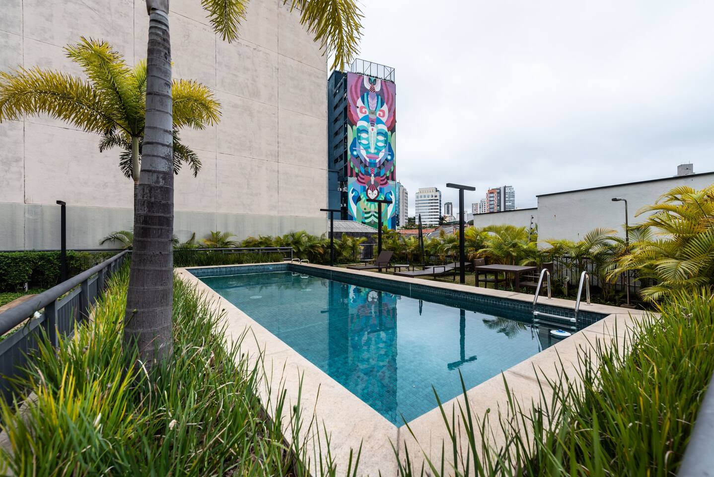 Piscina com paisagismo e arte urbana ao fundo, ambiente exclusivo.