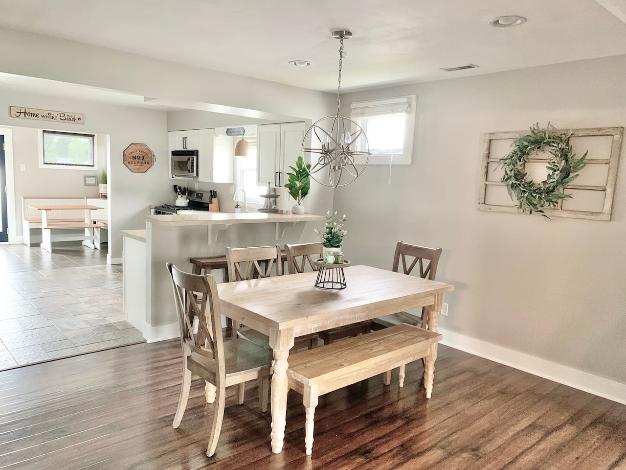 This inviting dining area features a rustic farmhouse table with bench seating and a striking orbital chandelier. The open layout provides a clear view of the kitchen and breakfast nook, making it easy to enjoy meals together during your stay.