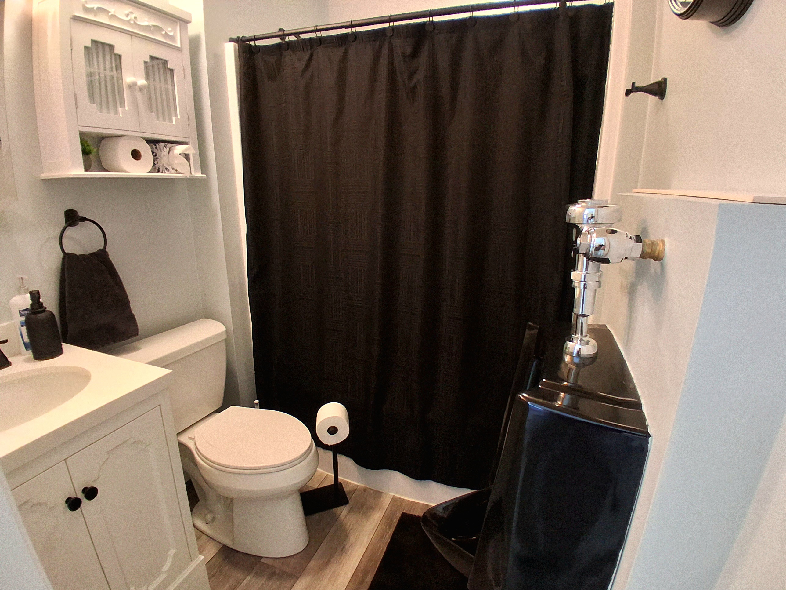 Designed for refined taste, this men’s bathroom features a sleek wall-mounted urinal, a mirrored Kohler medicine cabinet, and over-the-toilet storage. Black accents add bold contrast and modern polish to this calm, carefully curated space.