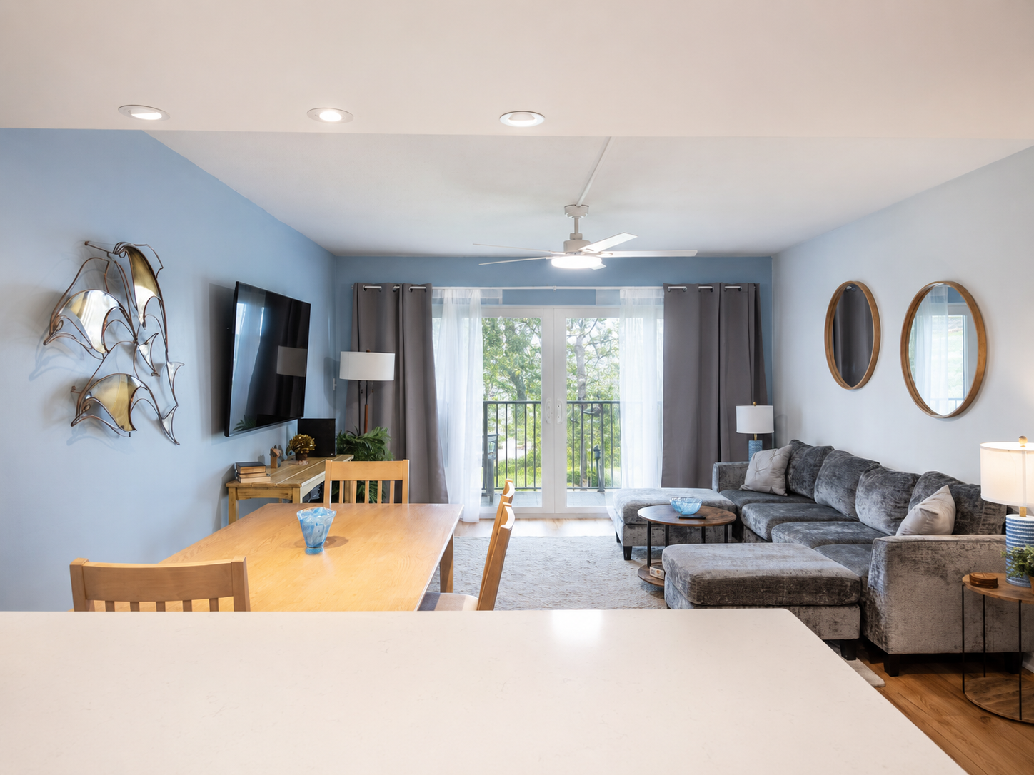 Modern living room with gray sectional, blue accent wall, and dining area view.