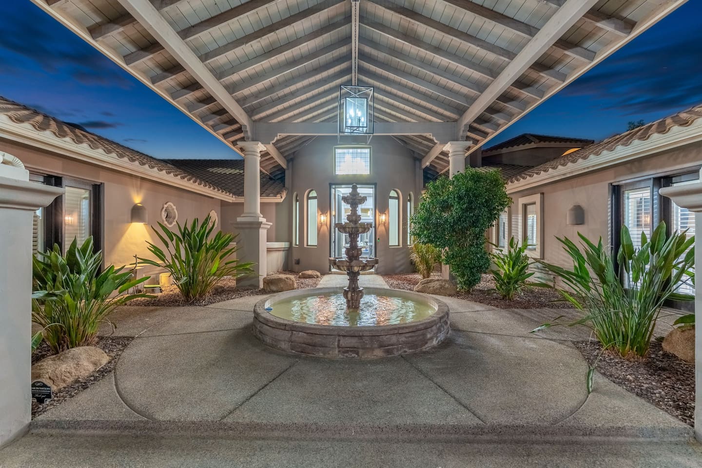 Step into sophistication with a serene courtyard featuring a tiered water fountain, lush greenery, and ambient lighting.

