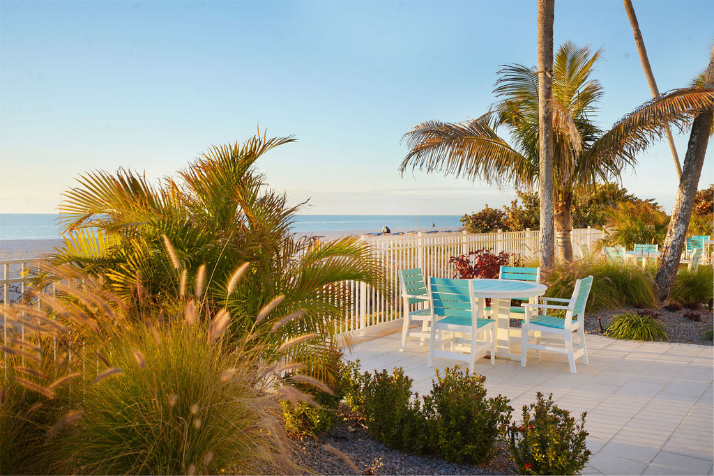 Outdoor seating area surrounded by tropical landscaping and palm trees, offering a peaceful space for al fresco dining, relaxation, and stunning beach views.