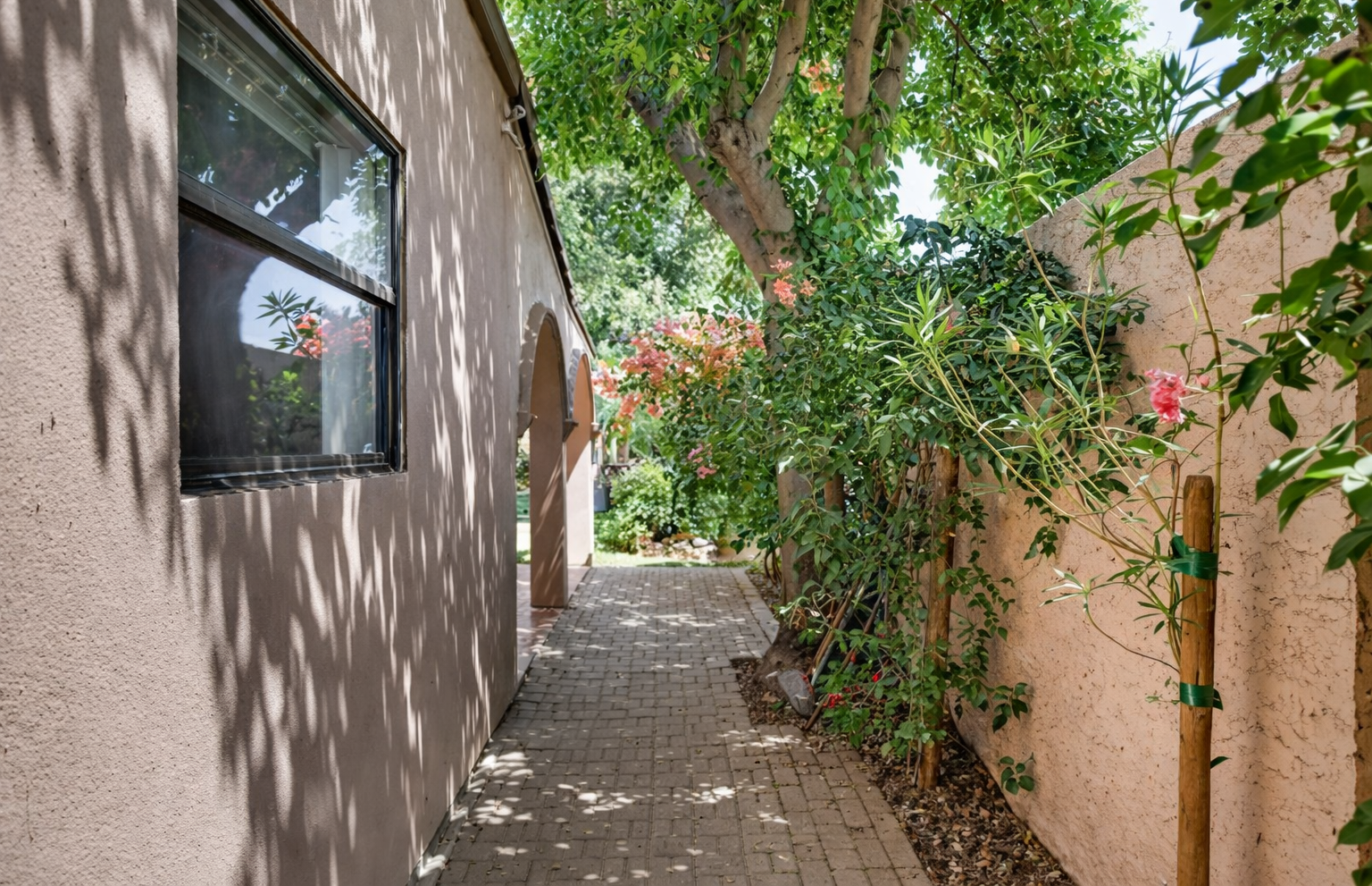A quiet garden walkway lined with flowers and trees creates a private, peaceful passage through the heart of the home.