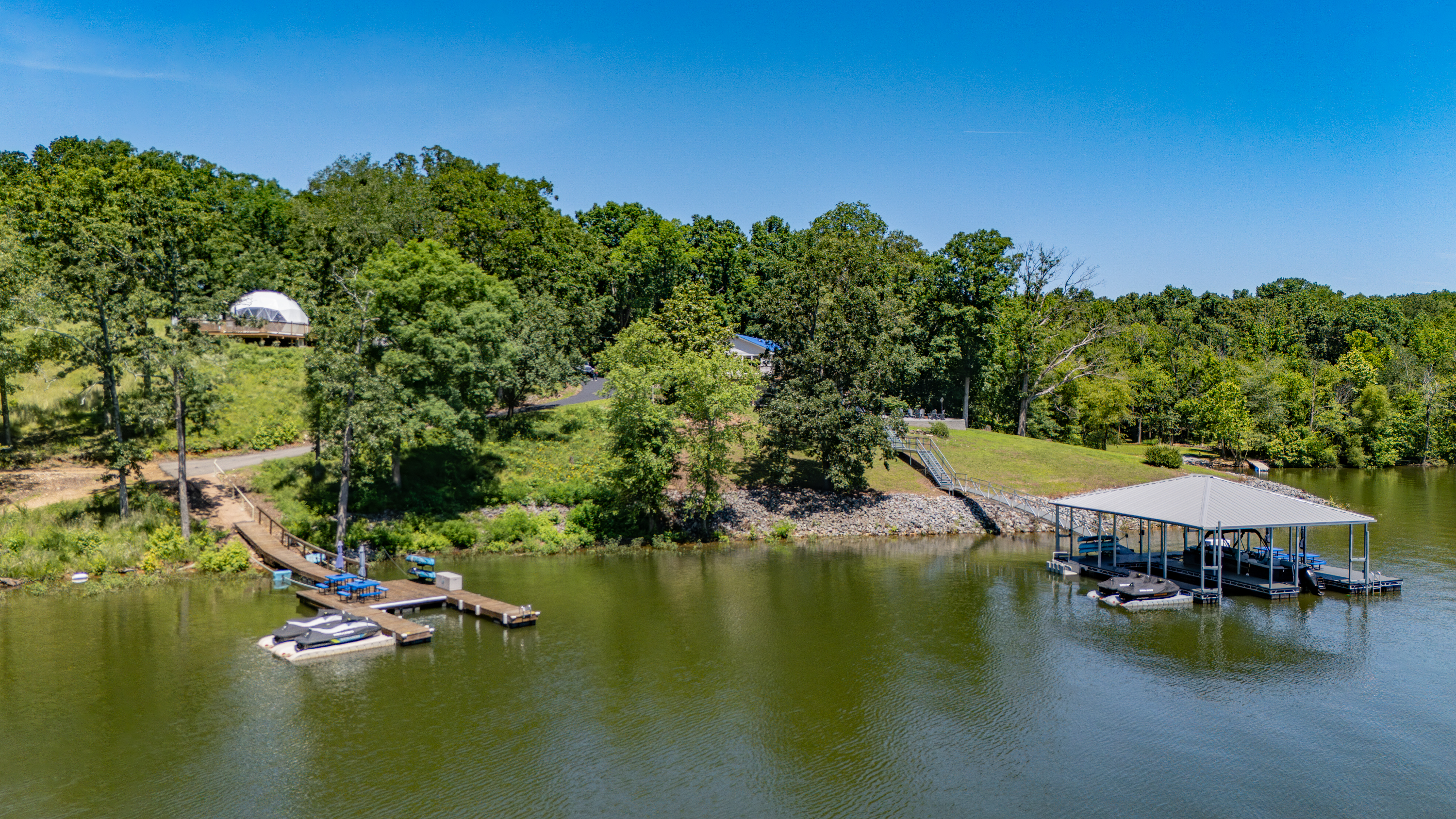 Aerial view of The View’s shoreline and private dock; the white Anchor Dome next door is visible beyond the trees.