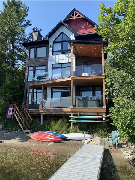 View of cottage from dock showing beach and watercraft; hottub on 1st balcony of cottage.