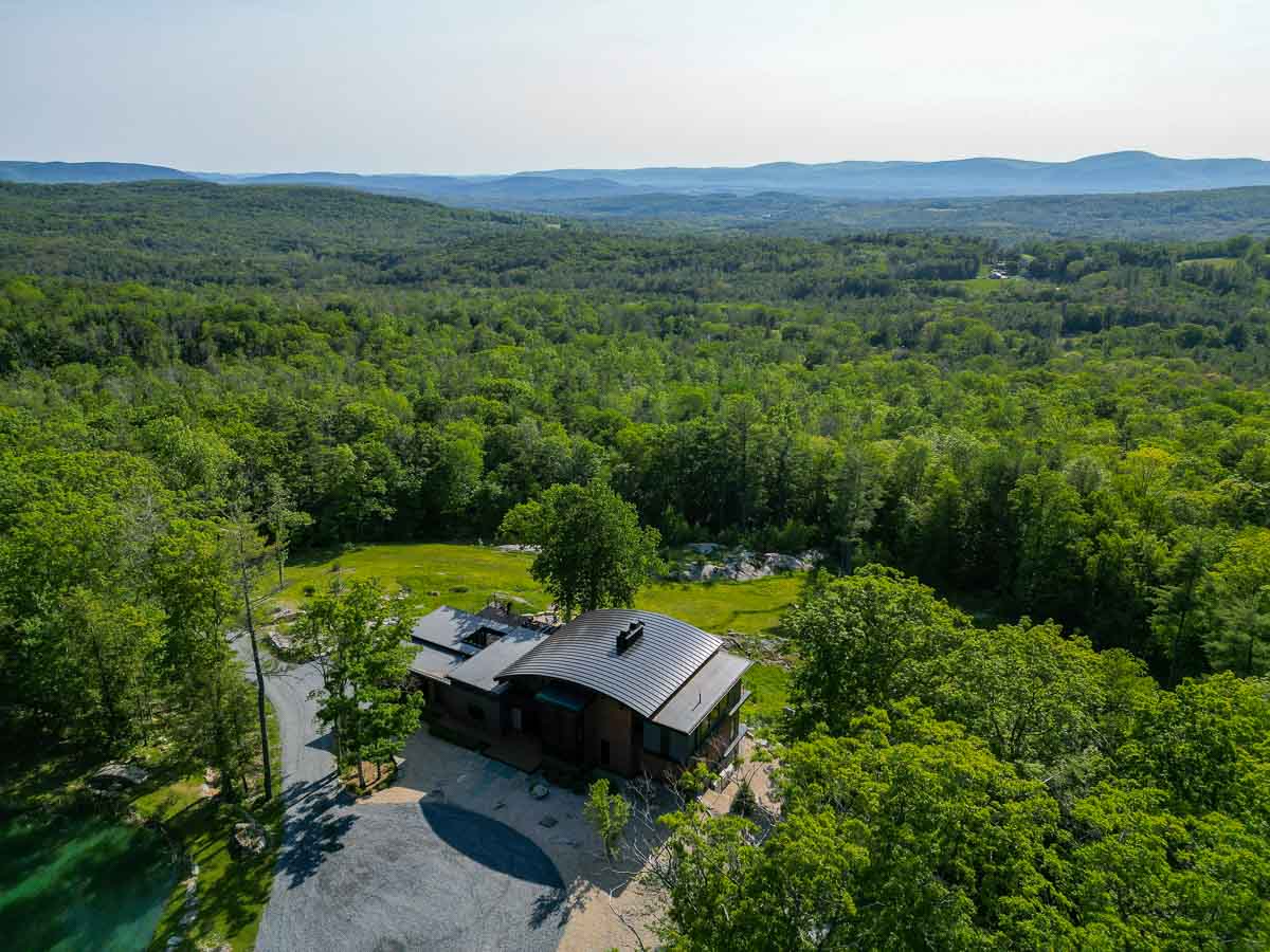 Aerial view of Sunset Falls Estate set into the Berkshires forest with mountain horizon