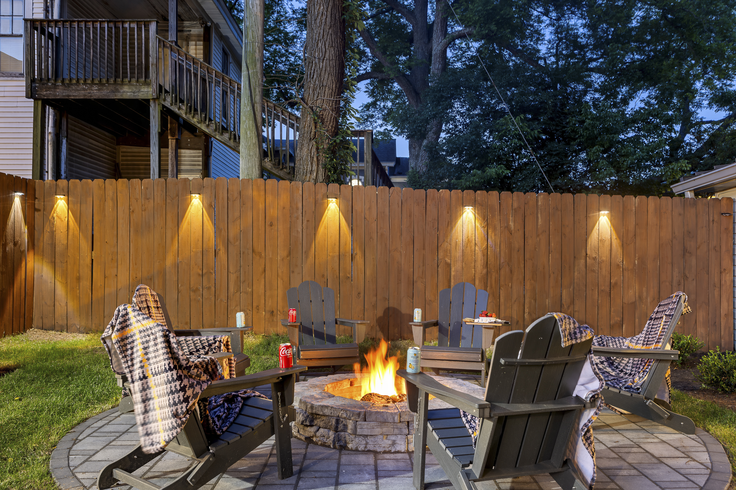 The backyard comes alive at night with warm lighting throughout, a crackling fire, and plenty of space for everyone to gather and relax.