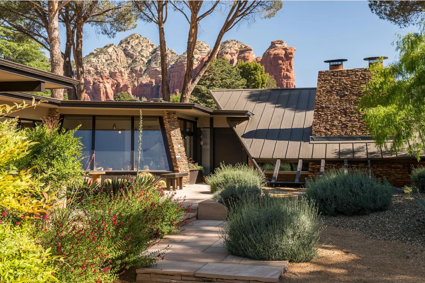 Inviting garden pathway leading to the home, bordered by vibrant desert landscaping and a distinctive stone chimney feature.
