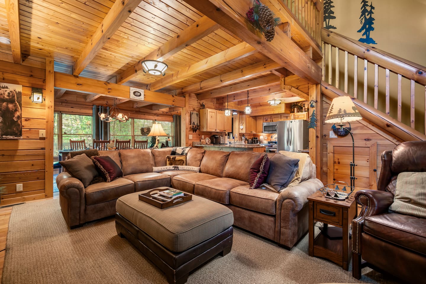 The open-concept main level features a living room with a spacious sectional and additional seating, an overlooking loft, and floor-to-ceiling wood interiors.