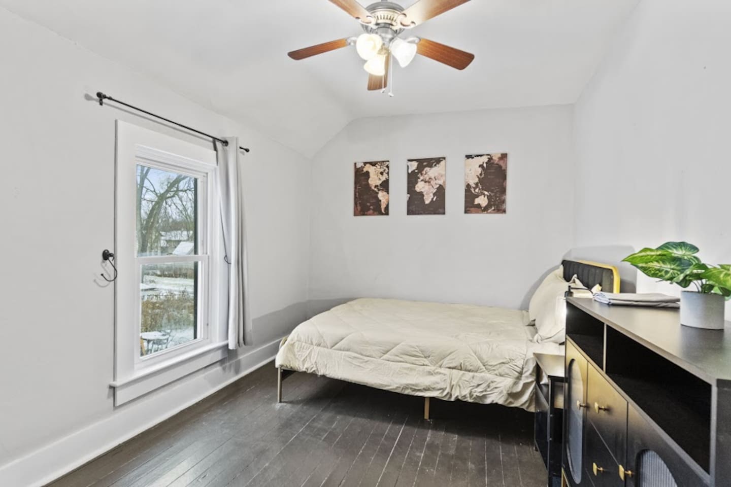 Chic bedroom featuring a luxurious bed, elegant decorations, a large window for natural light, a chandelier fan, and a stylish drawer with a table—designed to offer comfort and sophistication in a modern, airy space