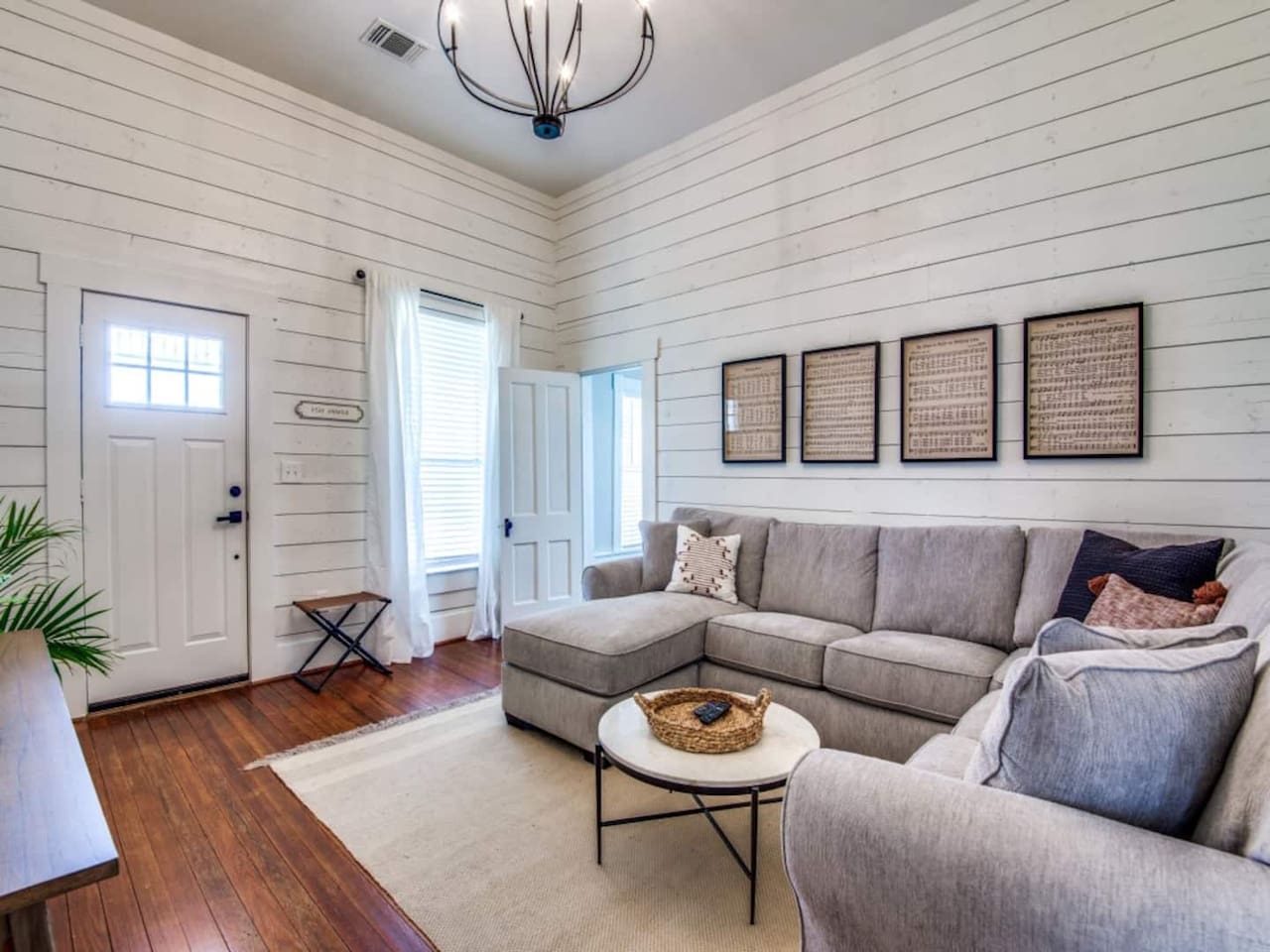 Sunlit shiplap living room with original hardwood floors, gray sectional, round coffee table, and large windows. Smart TV and high-speed Wi-Fi included. Modern farmhouse Airbnb in downtown Aubrey TX near Denton County wedding venues.