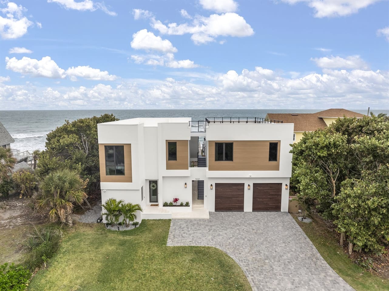 Take in the exterior view of this elegant home, featuring a welcoming door entrance, lush greenery, parking lots, sleek glass windows, and flooring. The house's vibrant color complements the stunning ocean views, offering a perfect sight-seeing spot.