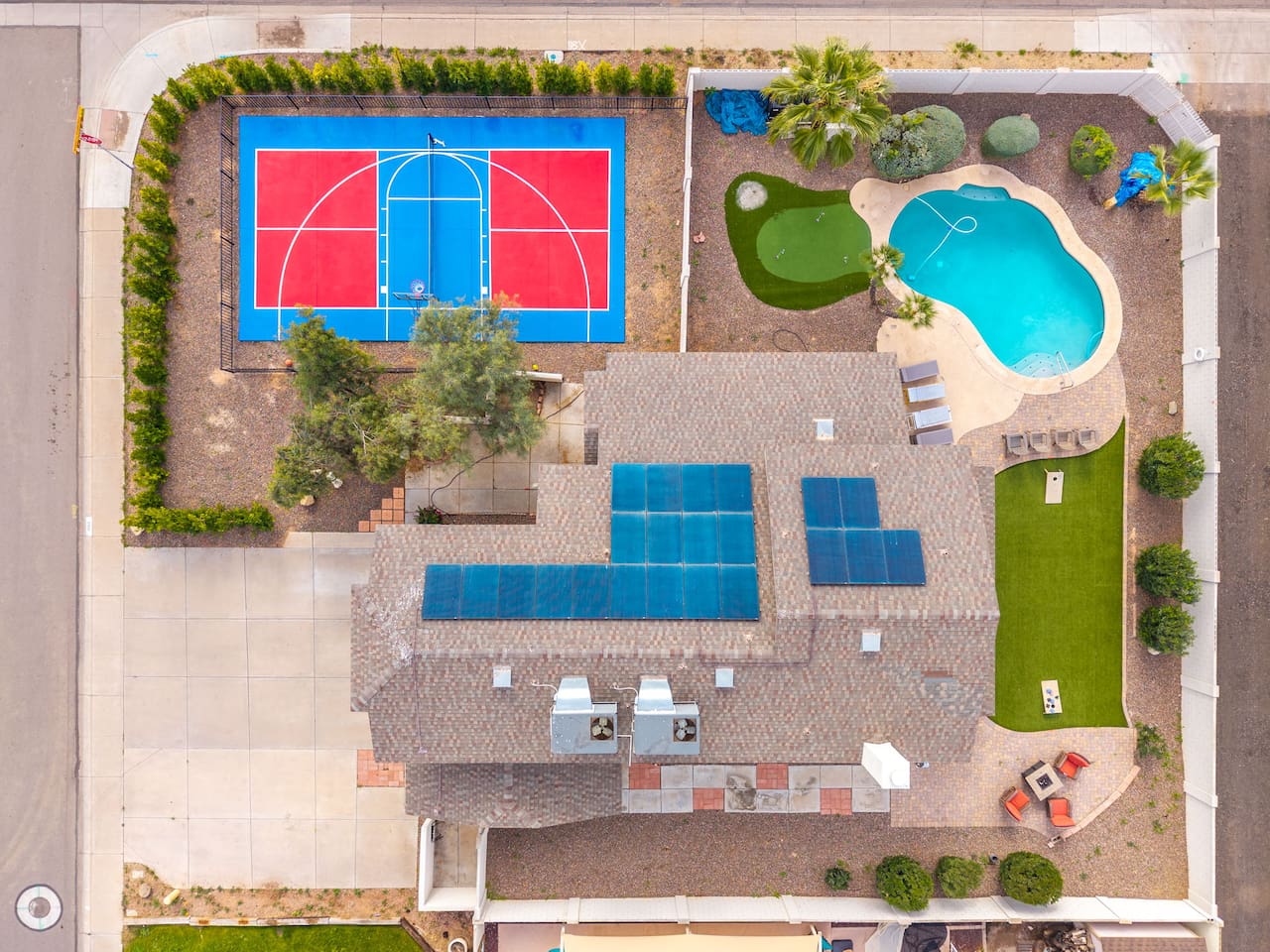 Aerial view of resort-style compound with basketball court, resort pool, solar panels, and sprawling grounds.