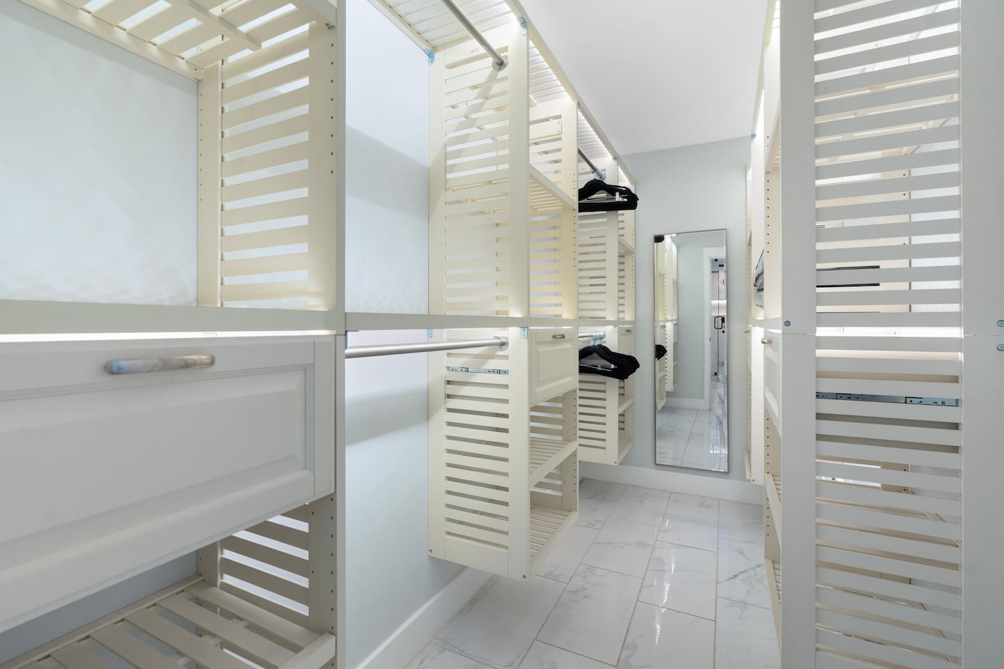 Keep everything organized with this thoughtfully designed walk-in closet featuring ample hanging space, drawers, and a full-length mirror.

